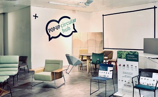 A room full of green furniture, with speech bubbles on the wall saying "Popup Circular Hub"