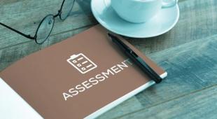 A leaflet titled Assessment on a table with a pen and a cup of coffee.
