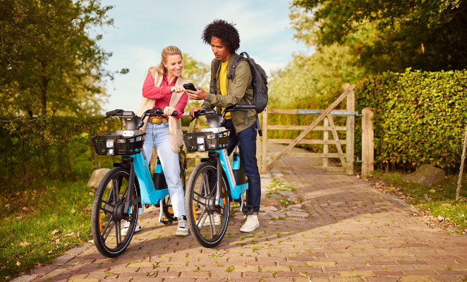 Two young people on a garden path, holding their bikes and looking at a mobile phone.