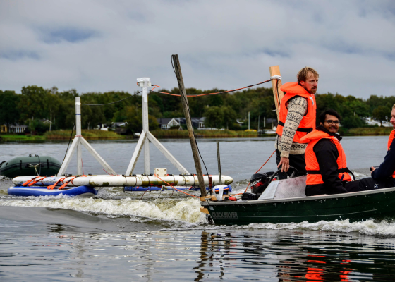 people in a boat with measuring material behind the boat on a lake.