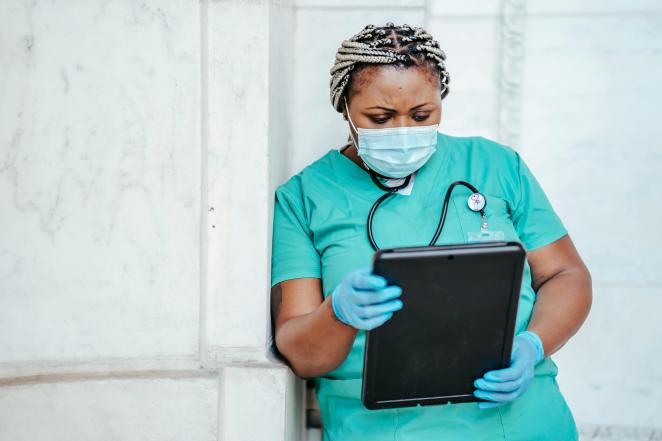 A nurse wearing a face mask holds a tablet, symbolising digital health solutions in healthcare. 