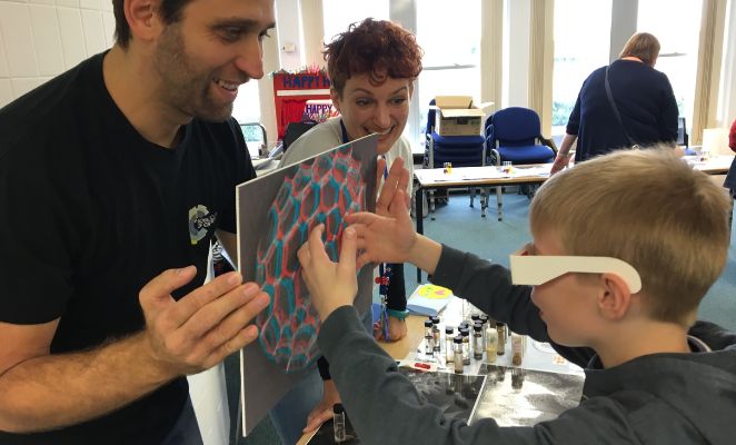 A school boy wearing VR glasses is touching an image held up by a teacher.