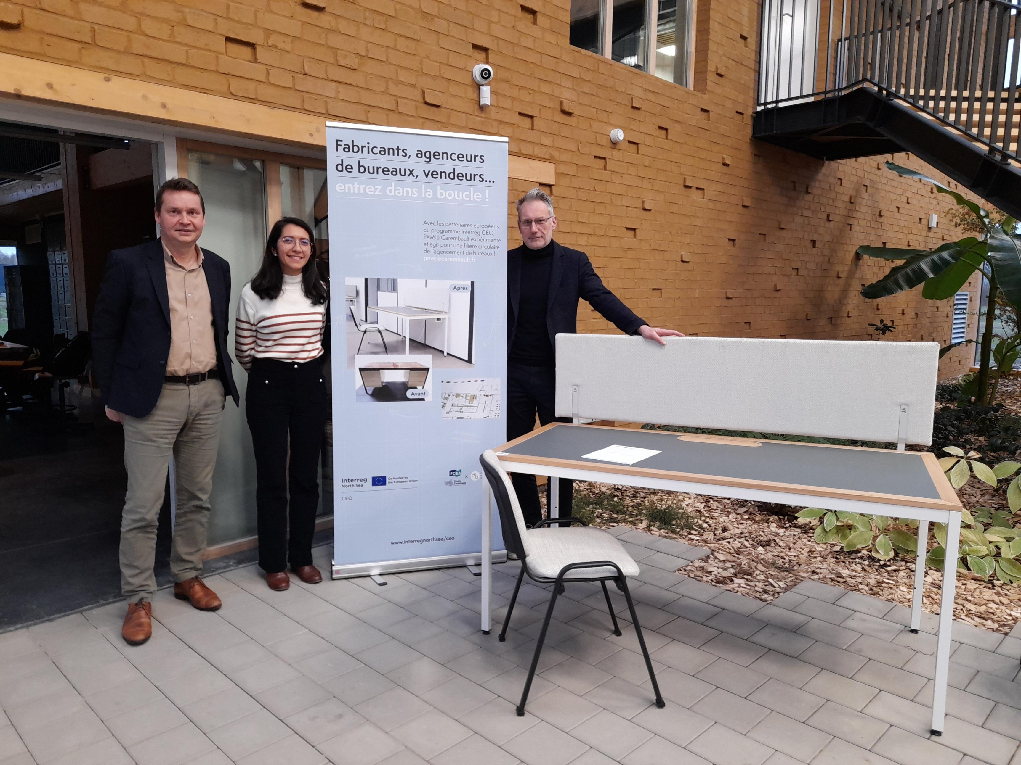 Three people from the France pilot standing in front of building next to poster