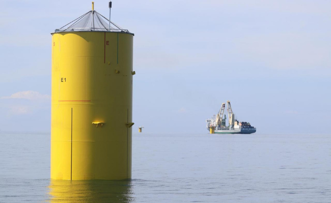 A large yellow cylindrical construction in the sea, with a ship at a distance. 