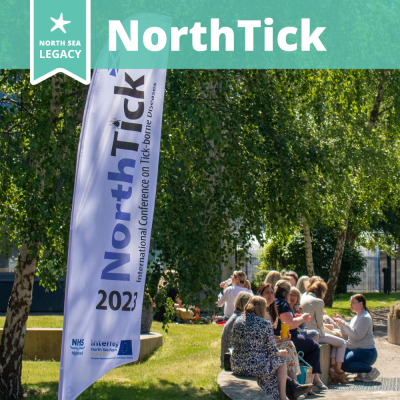 People seated outdoors next to a large beach flag saying NorthTick