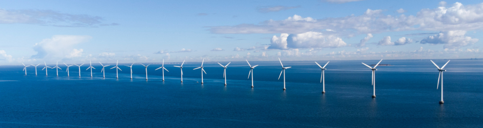 A row of white wind turbines in the dark blue North Sea in calm weather.