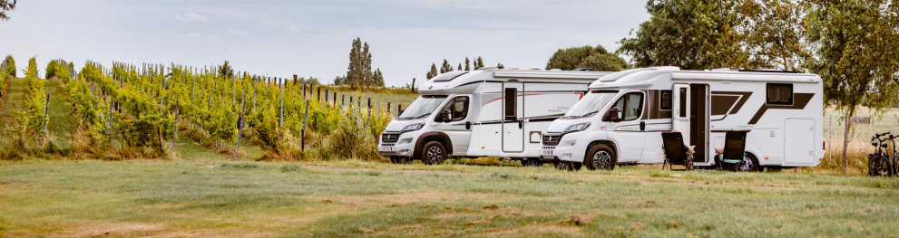 A campsite in West-Vlaanderen with a winery in the background and two caravans in the foreground. 